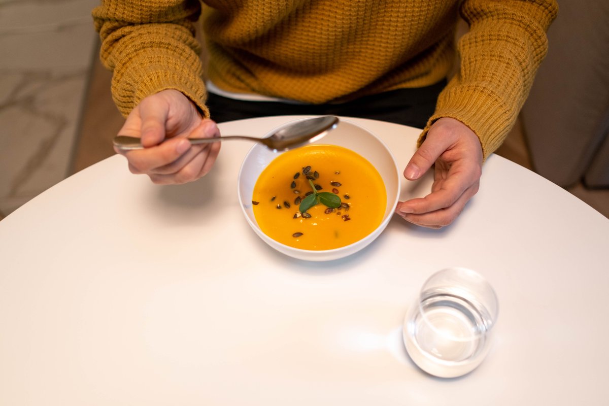 Bowl of smooth pumpkin soup and a glass of water on a white table