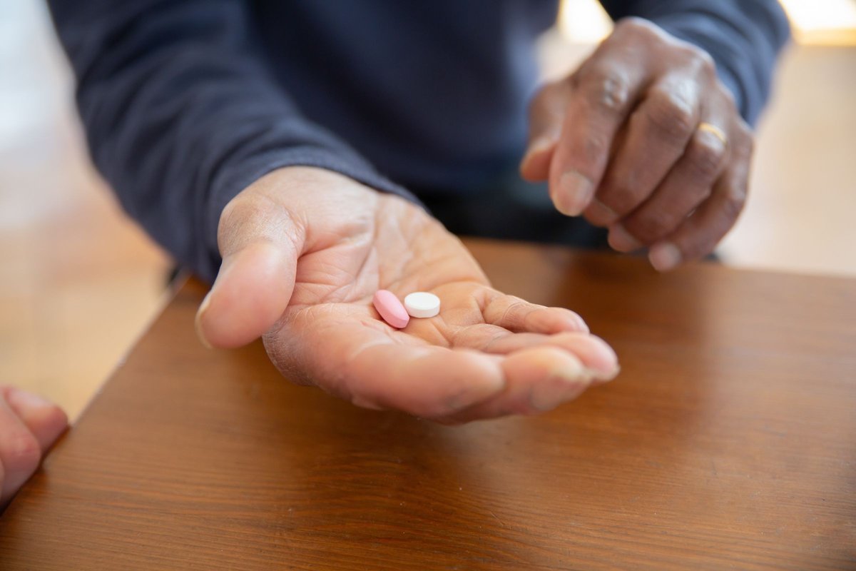 Older man holding two tablets in his open hand at a wooden table
