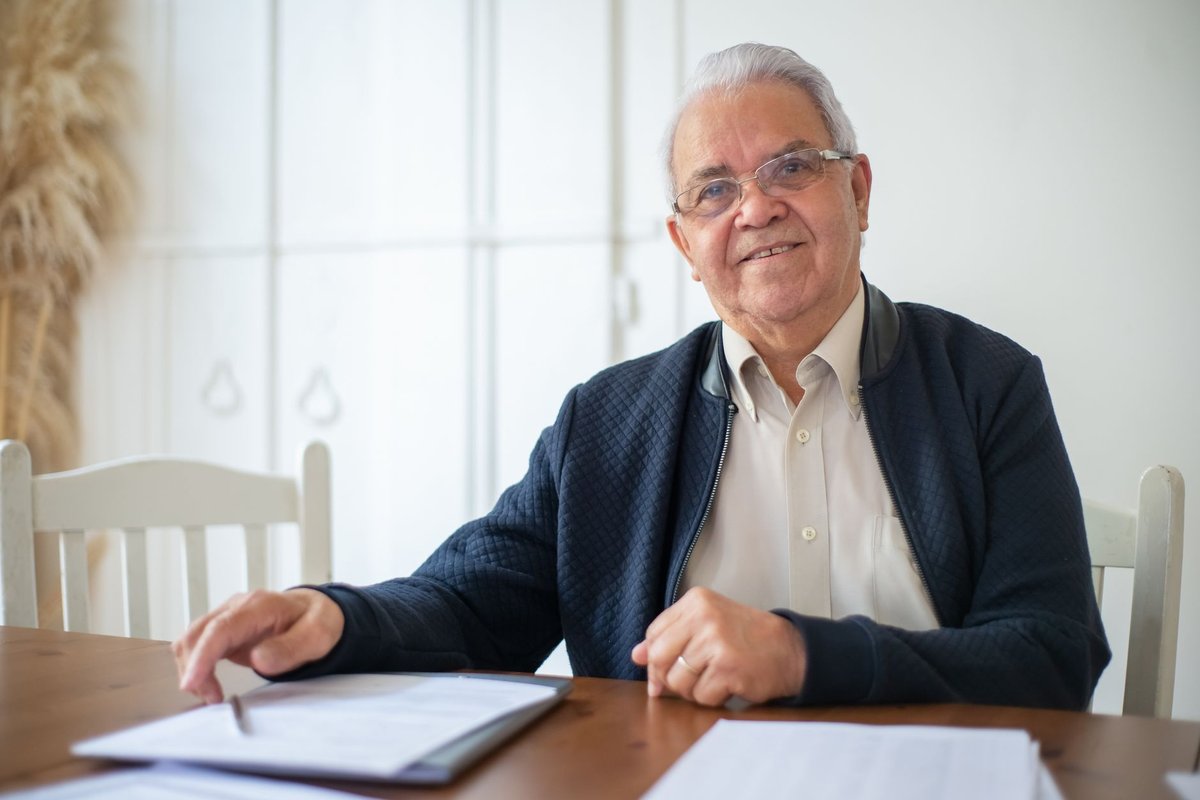 Smiling older man seated at a table with a folder of documents in front of him
