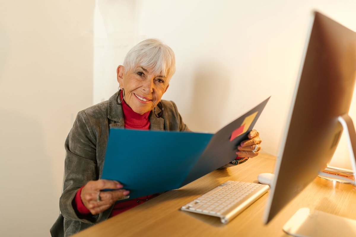 Smiling older woman holding an open folder of records at her desk