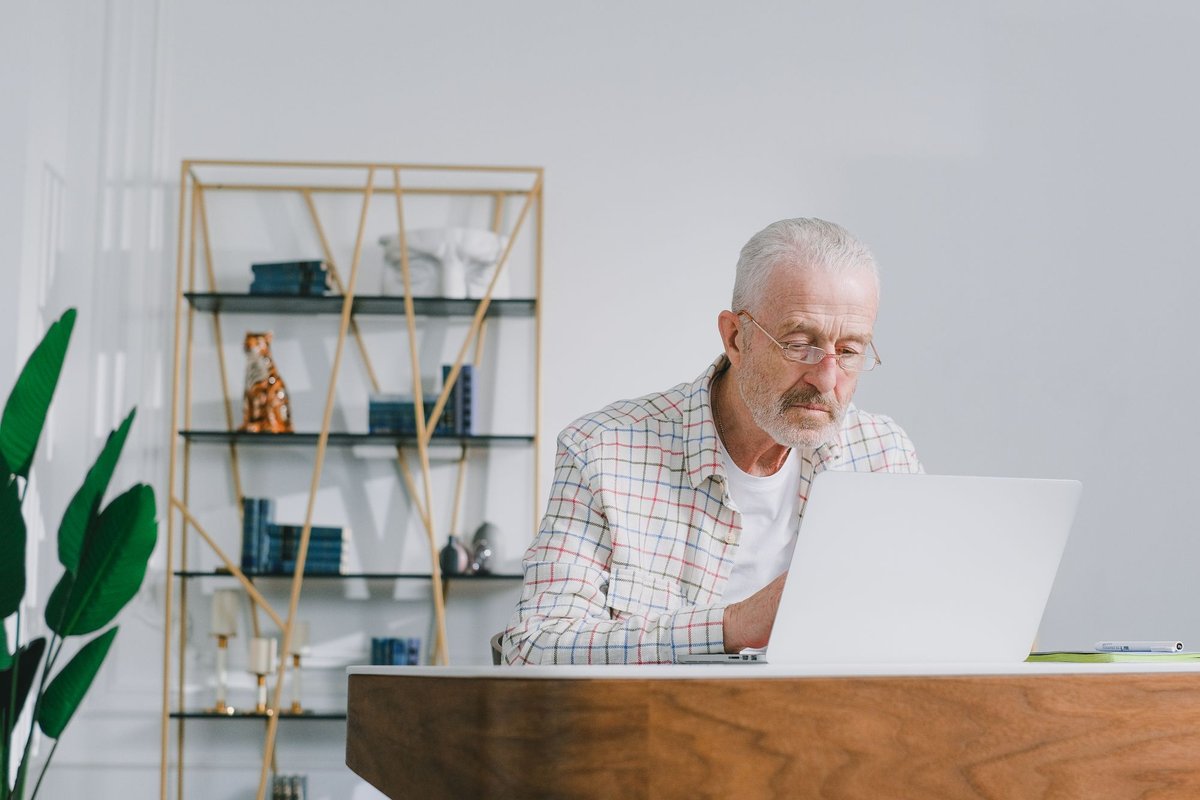 Older man with glasses sitting at a desk looking carefully at his laptop screen