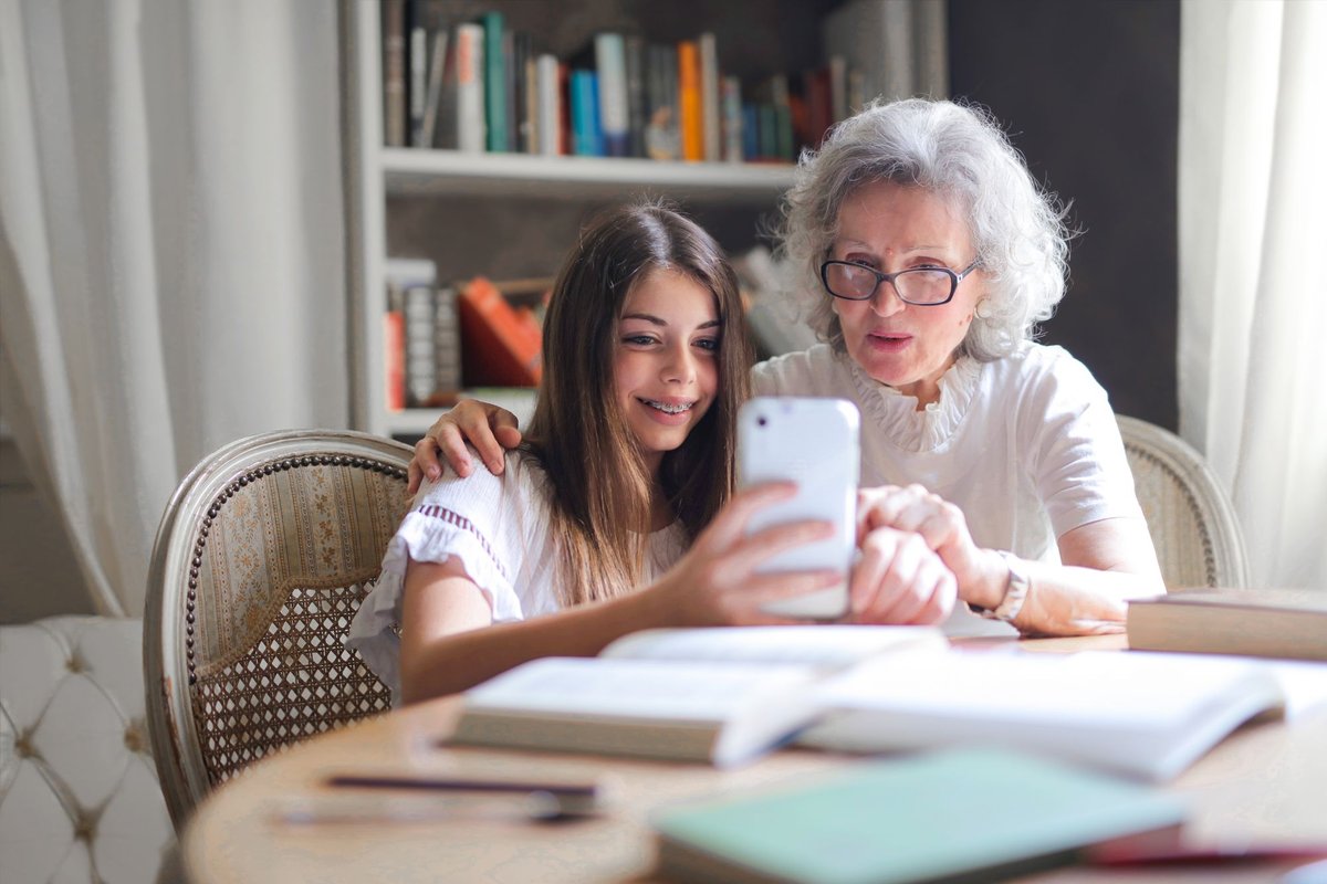 Smiling girl and her grandmother with glasses looking at a smartphone together at a table