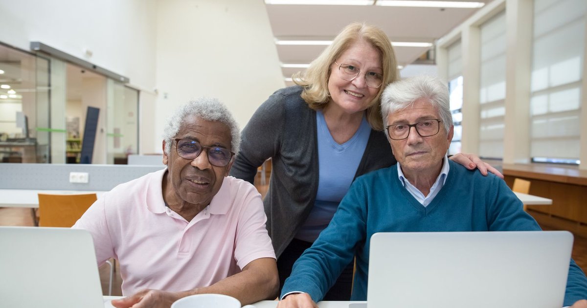 Three older adults smiling during a computer class in a bright community room