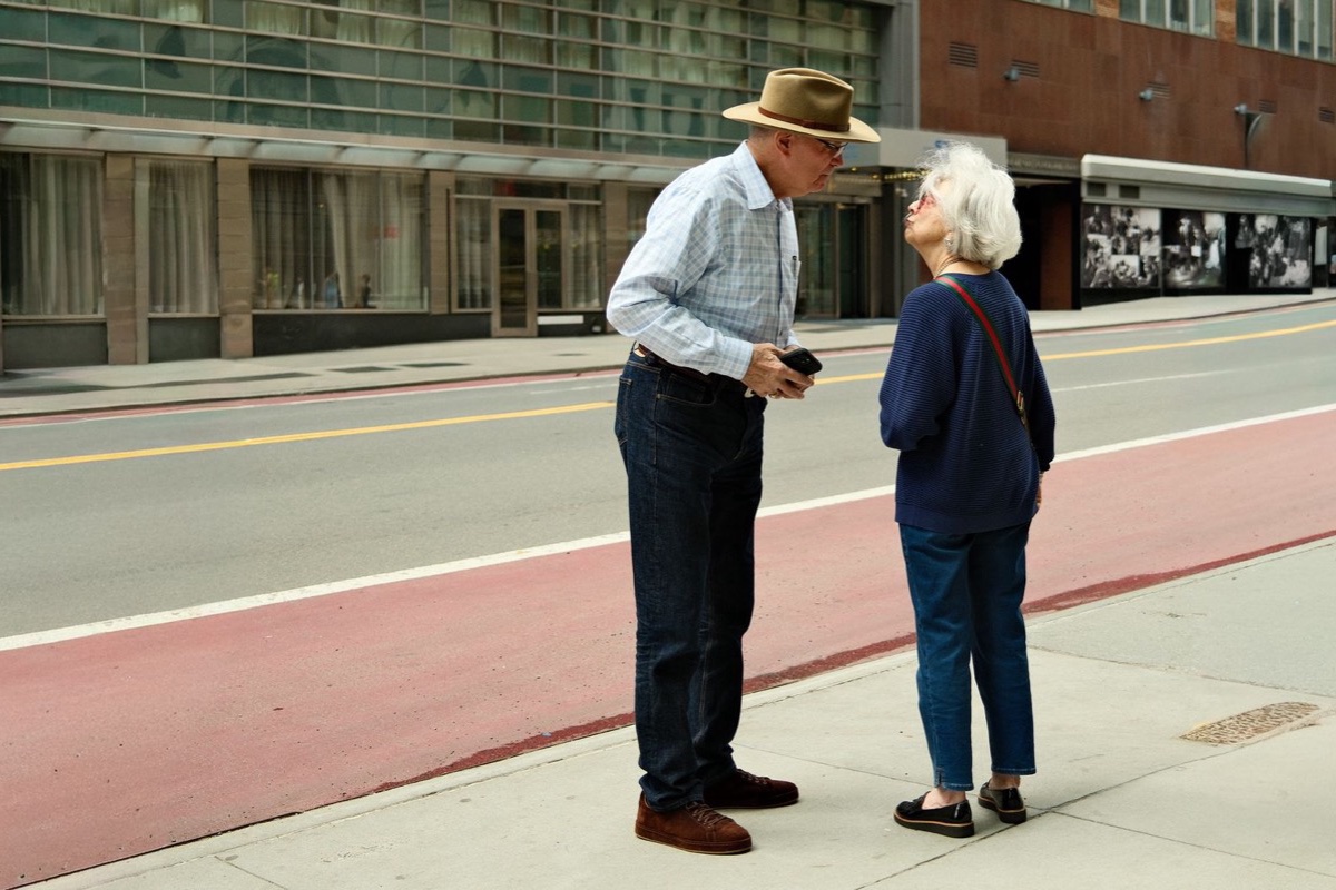 Older couple talking on a city sidewalk beside a red bus lane