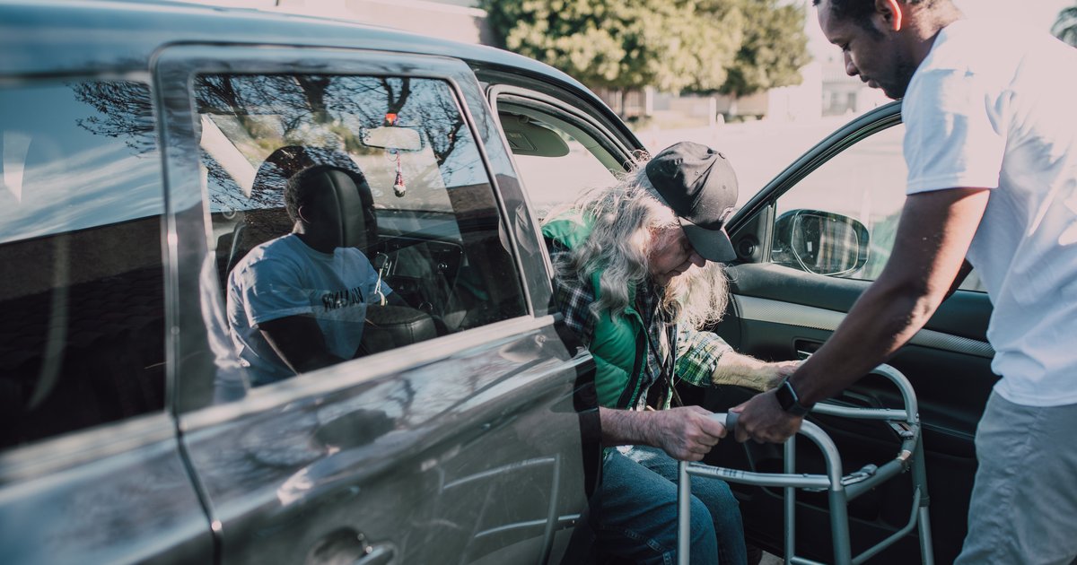 Man helping an older adult with a walker out of a car