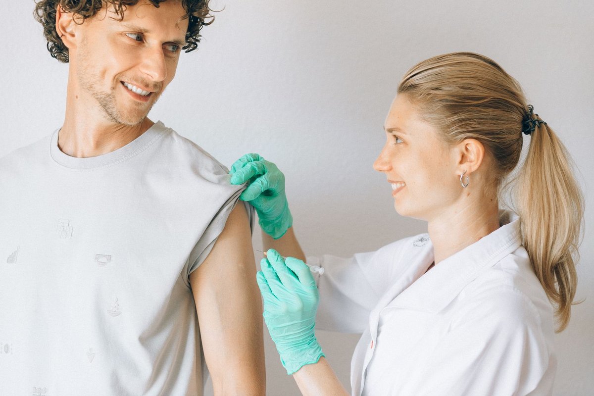 Smiling nurse in gloves giving a vaccine shot to a smiling patient indoors