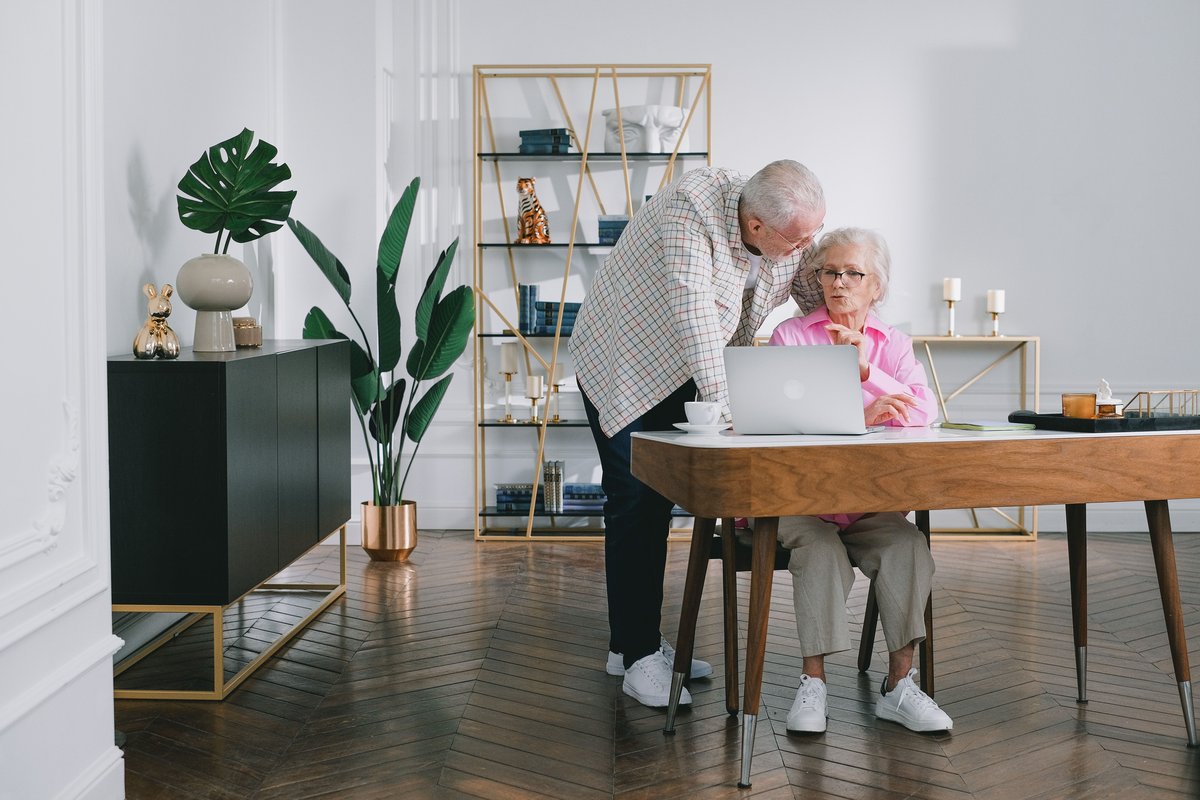 Older man and woman at a desk looking together at a laptop in a bright room