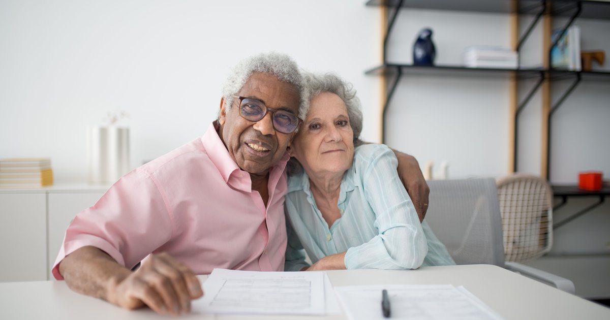Smiling older couple sitting close together at a table with forms in front of them