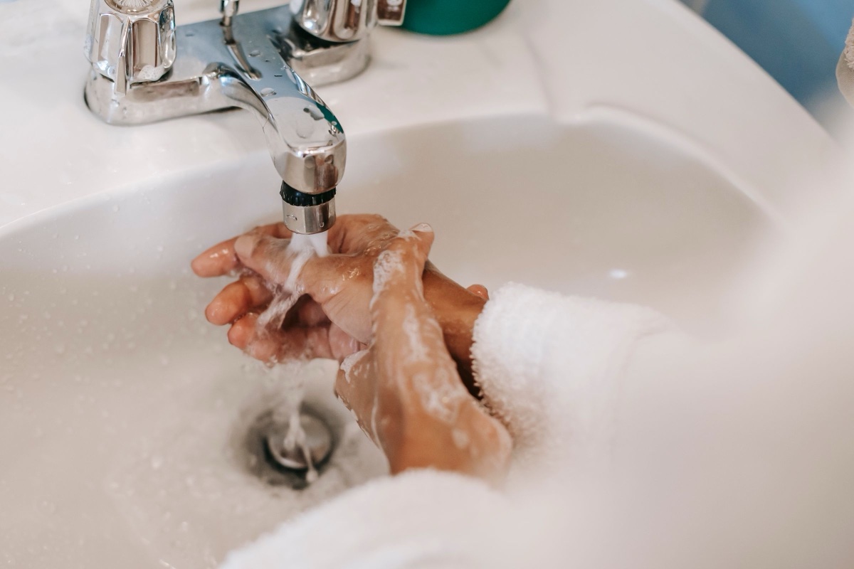 Hands being washed with soap under running water at a white bathroom sink