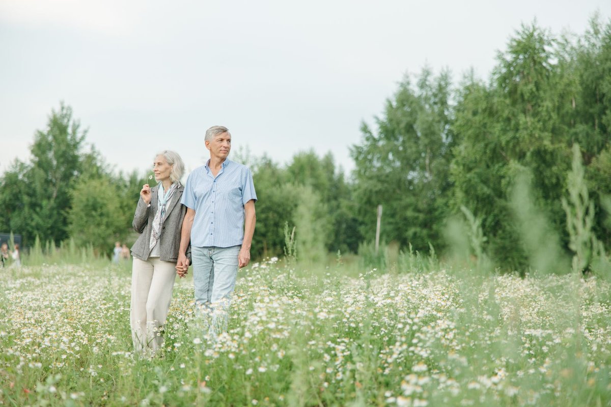 Older couple holding hands on a walk through a green meadow with white flowers