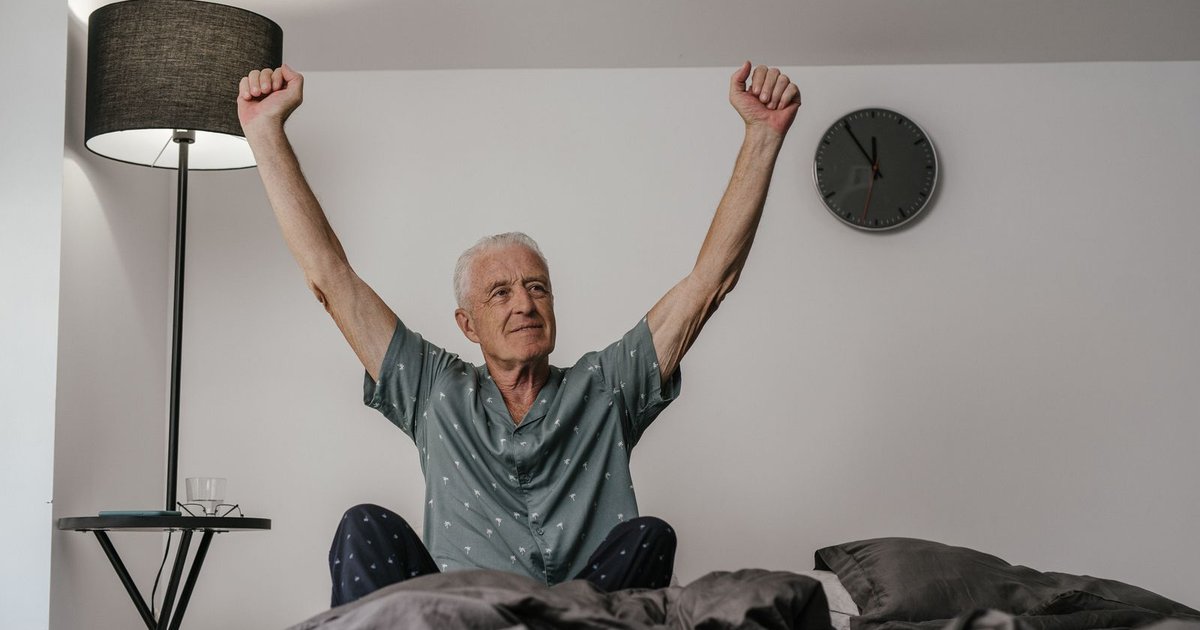 Smiling older man in pajamas stretching his arms as he wakes up in a bright bedroom