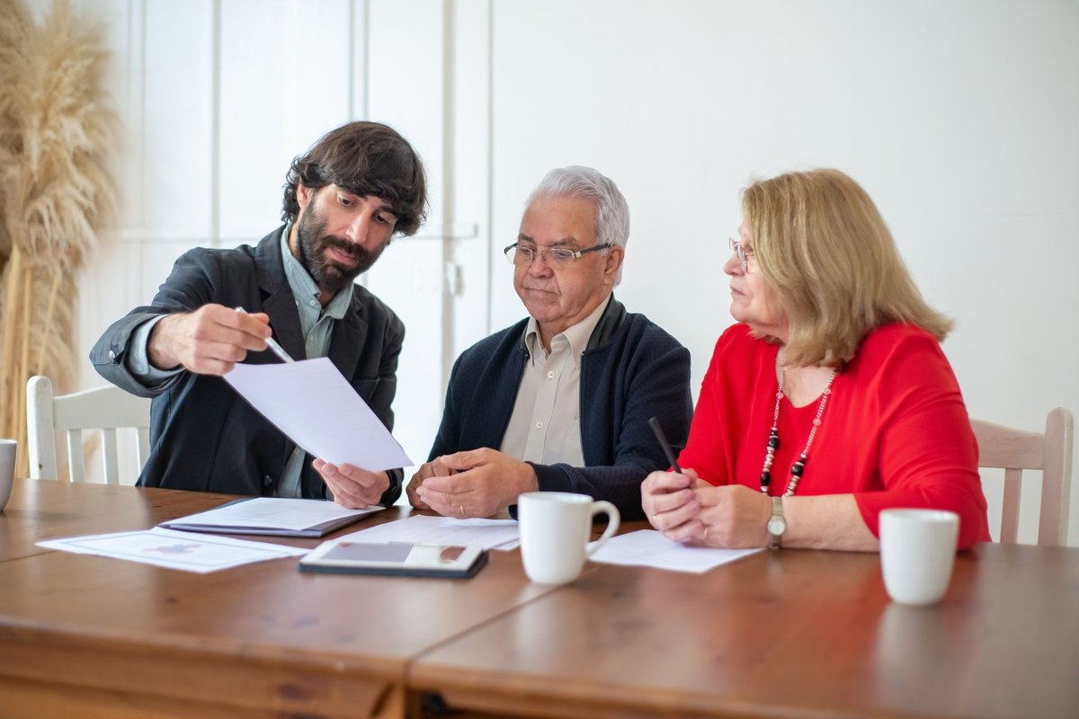 Older couple at a wooden table reviewing papers with an advisor who points to a page