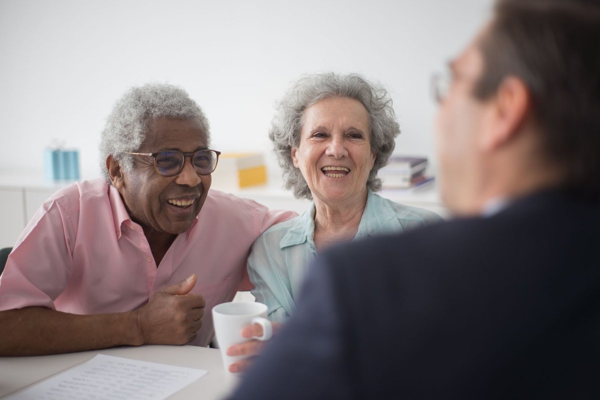 Smiling older couple talking with an advisor across a table with a cup of coffee