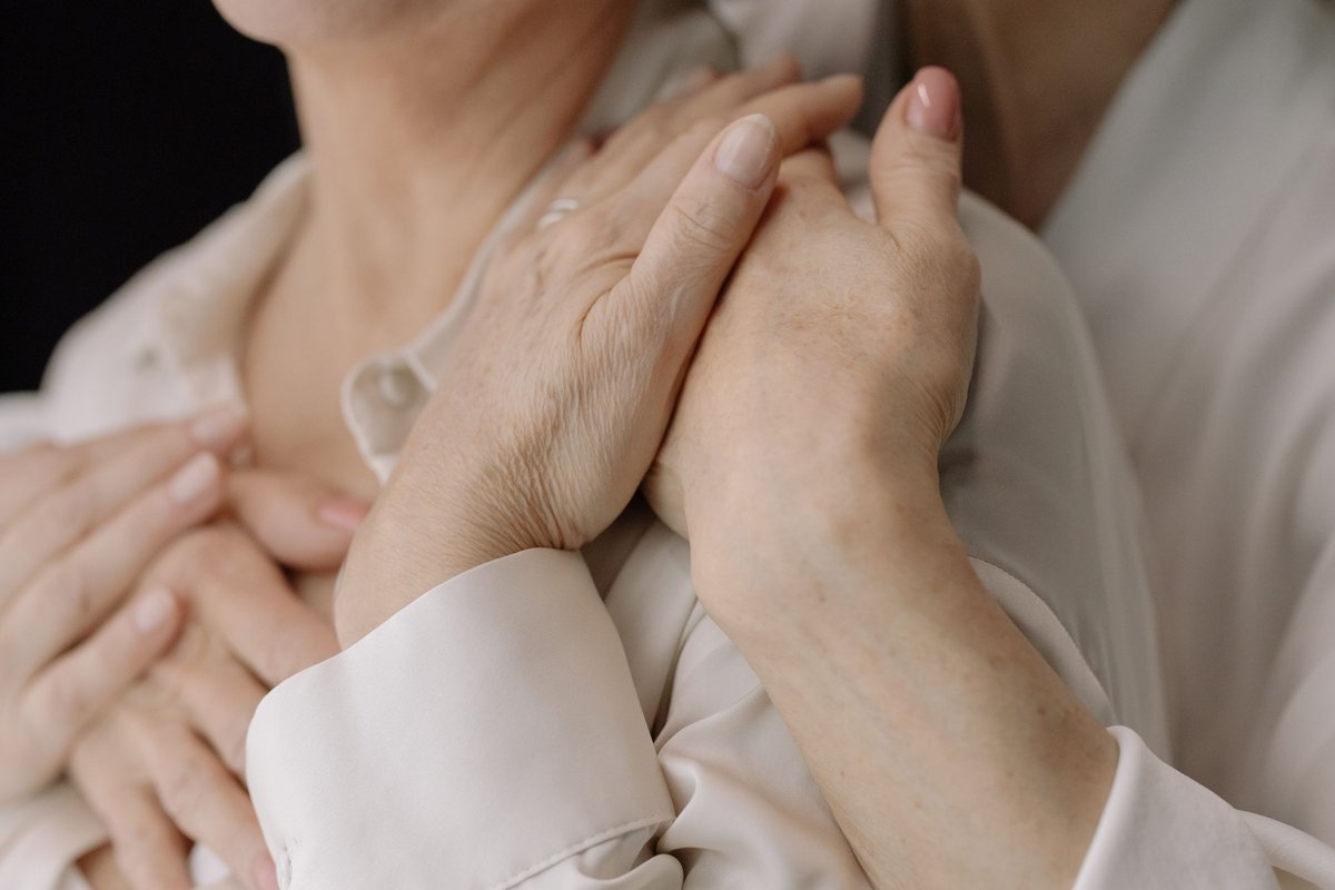 Close-up of two older women's hands resting together in a gesture of comfort