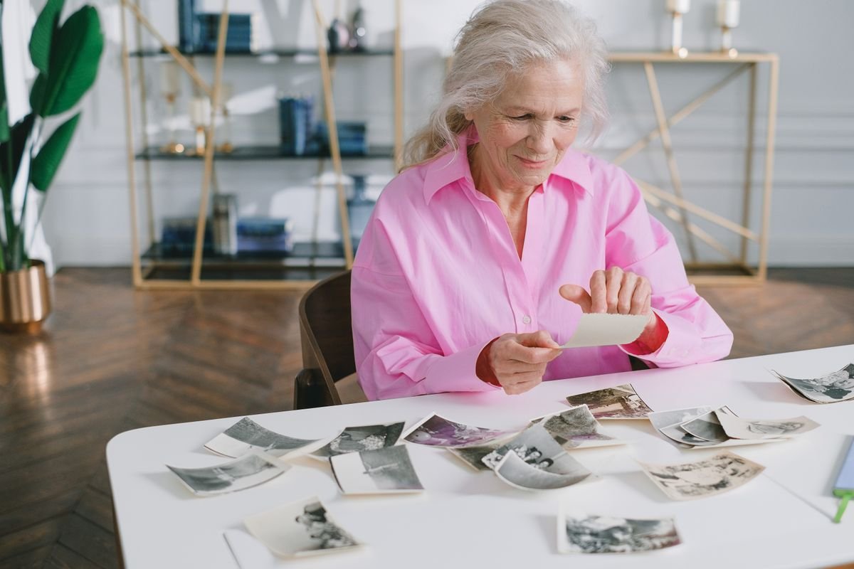 Older woman smiling while sorting old black and white photographs at a table