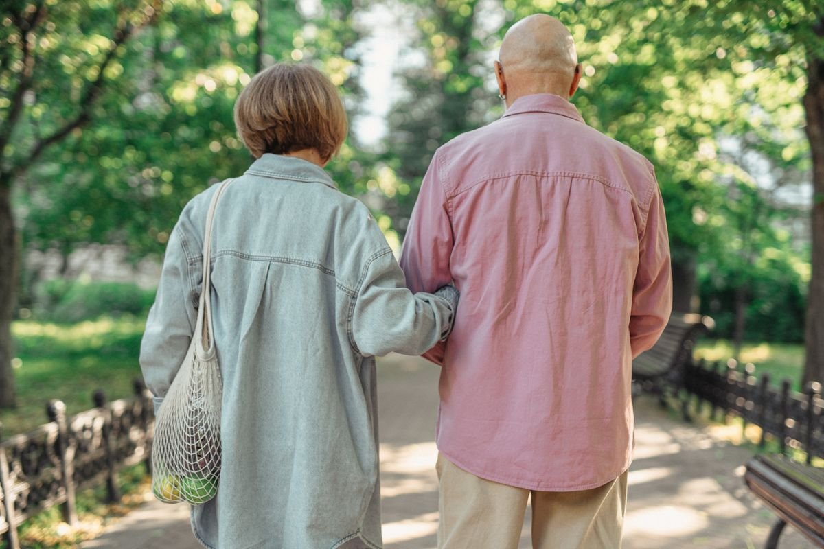 Older couple walking arm in arm along a sunlit park path