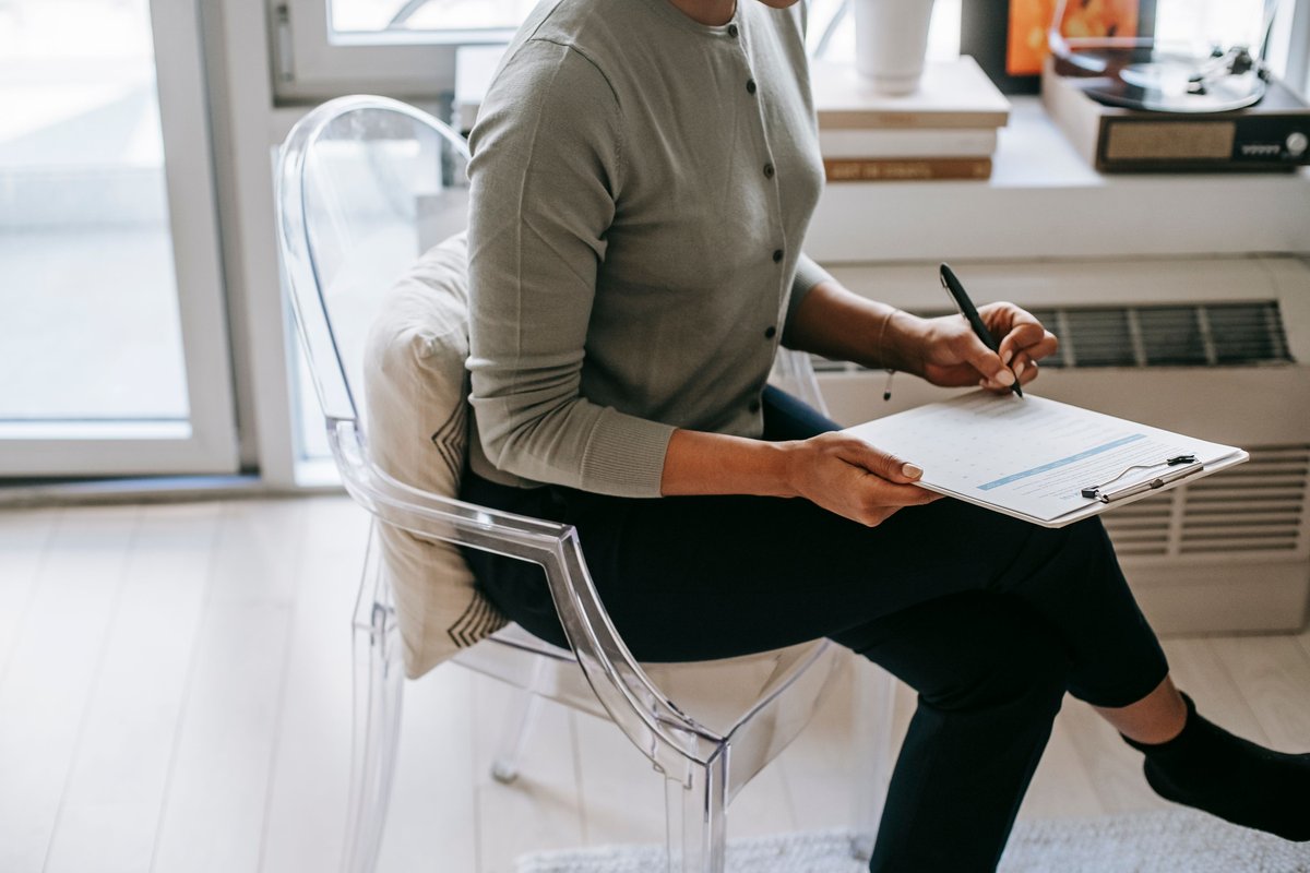 Person seated by a window filling out a form on a clipboard