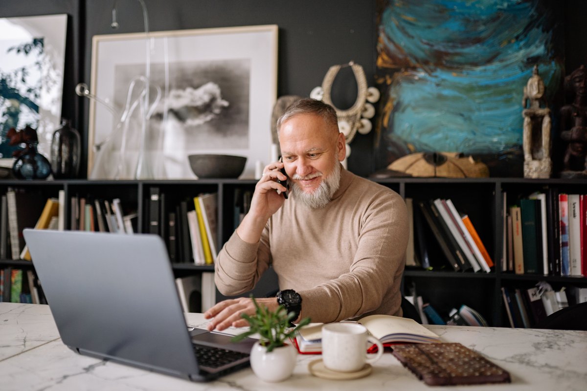 Man talking on the phone with a laptop open on a marble table at home