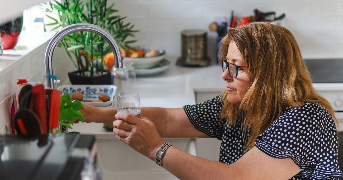 Woman with glasses filling a glass of water at a kitchen tap
