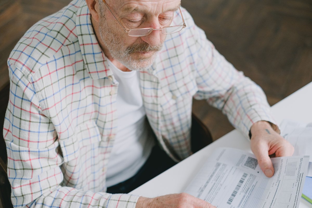 Older man with glasses reading a printed form at a table