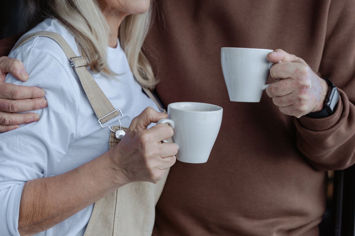 Older couple standing close together holding white mugs of tea