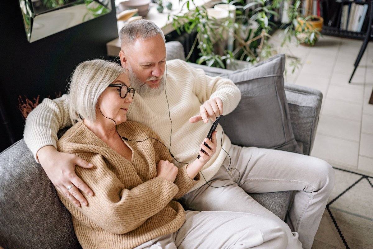 Older couple on a sofa sharing earphones and listening to music from a phone