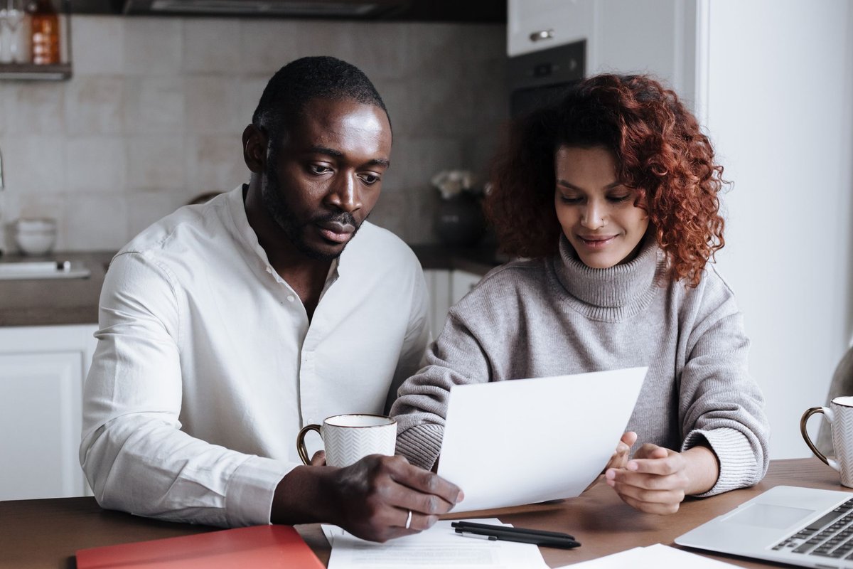 Couple reviewing a paper document together at a kitchen table with a laptop