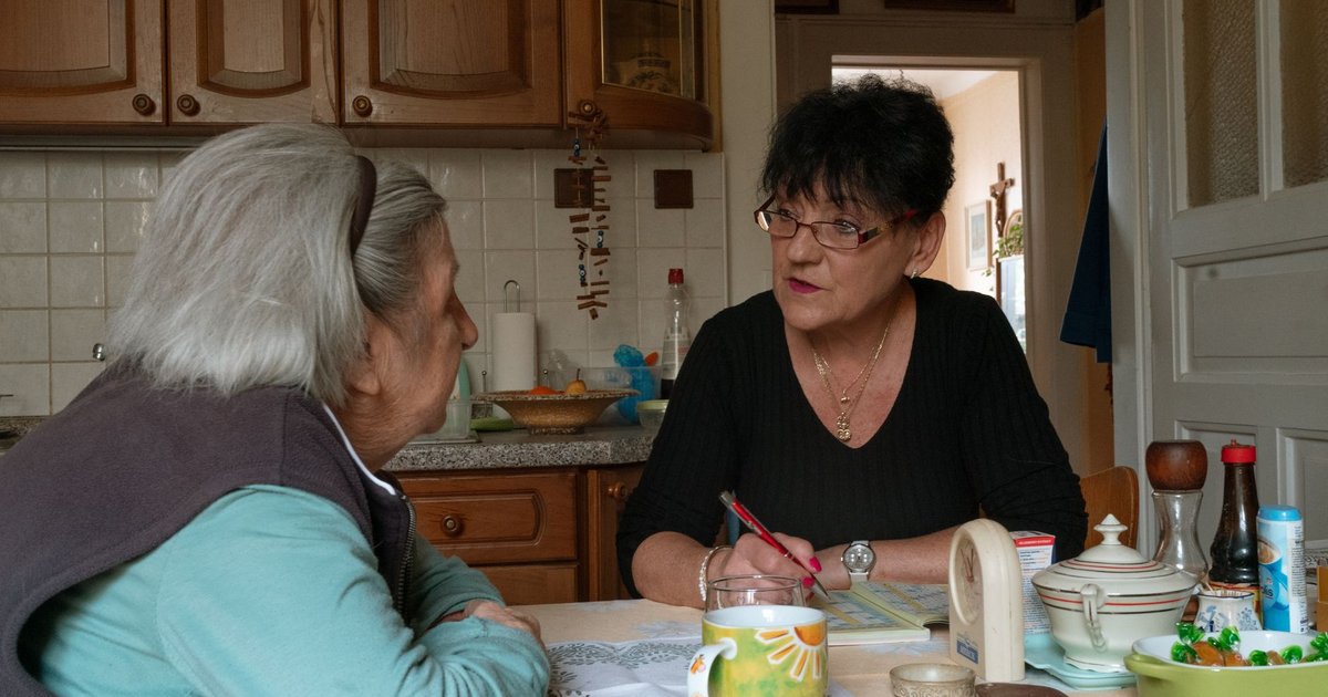 Care manager taking notes while talking with an older woman at her kitchen table