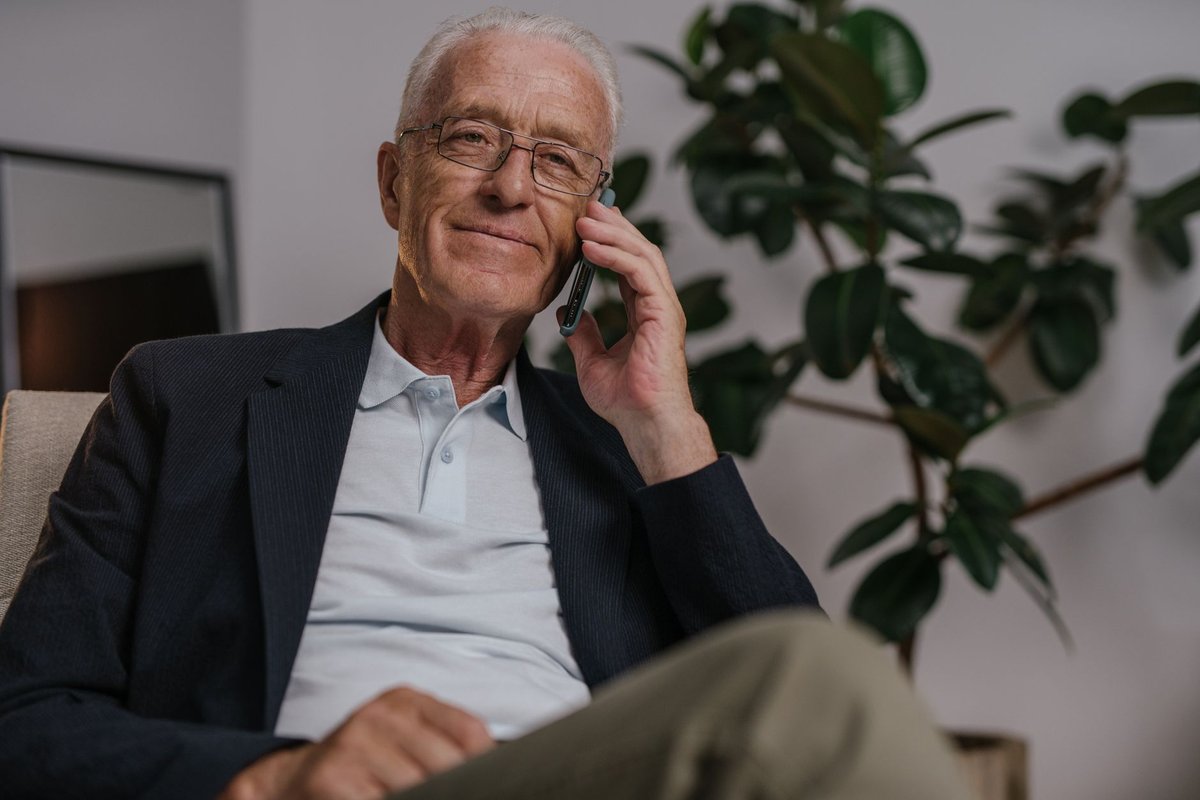 Smiling older man with glasses talking on a mobile phone in an armchair at home
