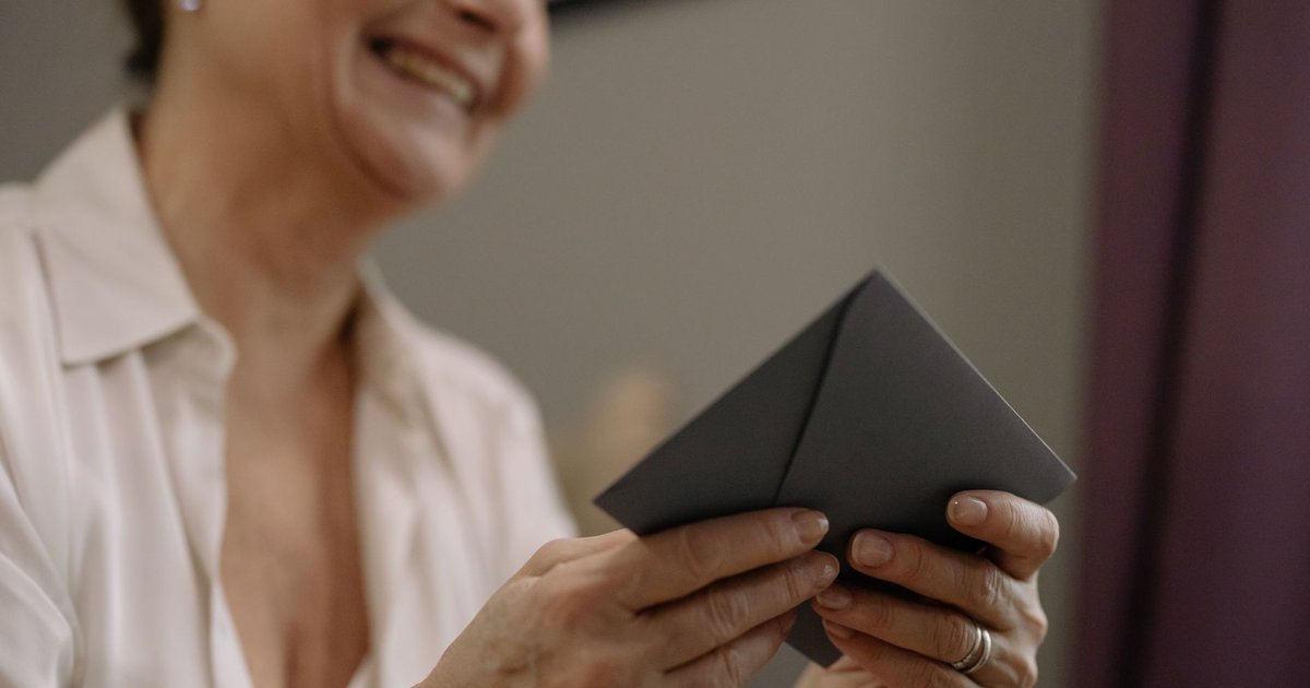Smiling older woman holding a gray envelope in both hands at home