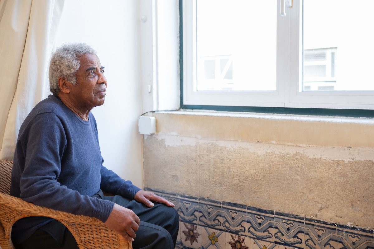 Older man sitting in a wicker chair looking thoughtfully out of a window