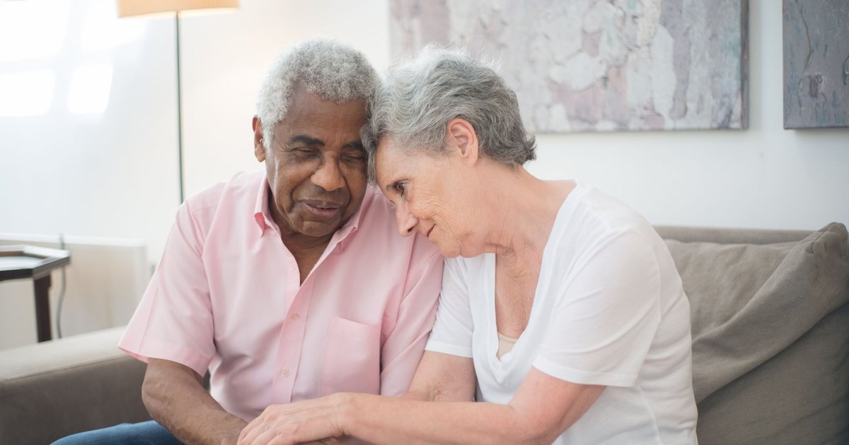 Older couple sitting close together on a sofa holding hands
