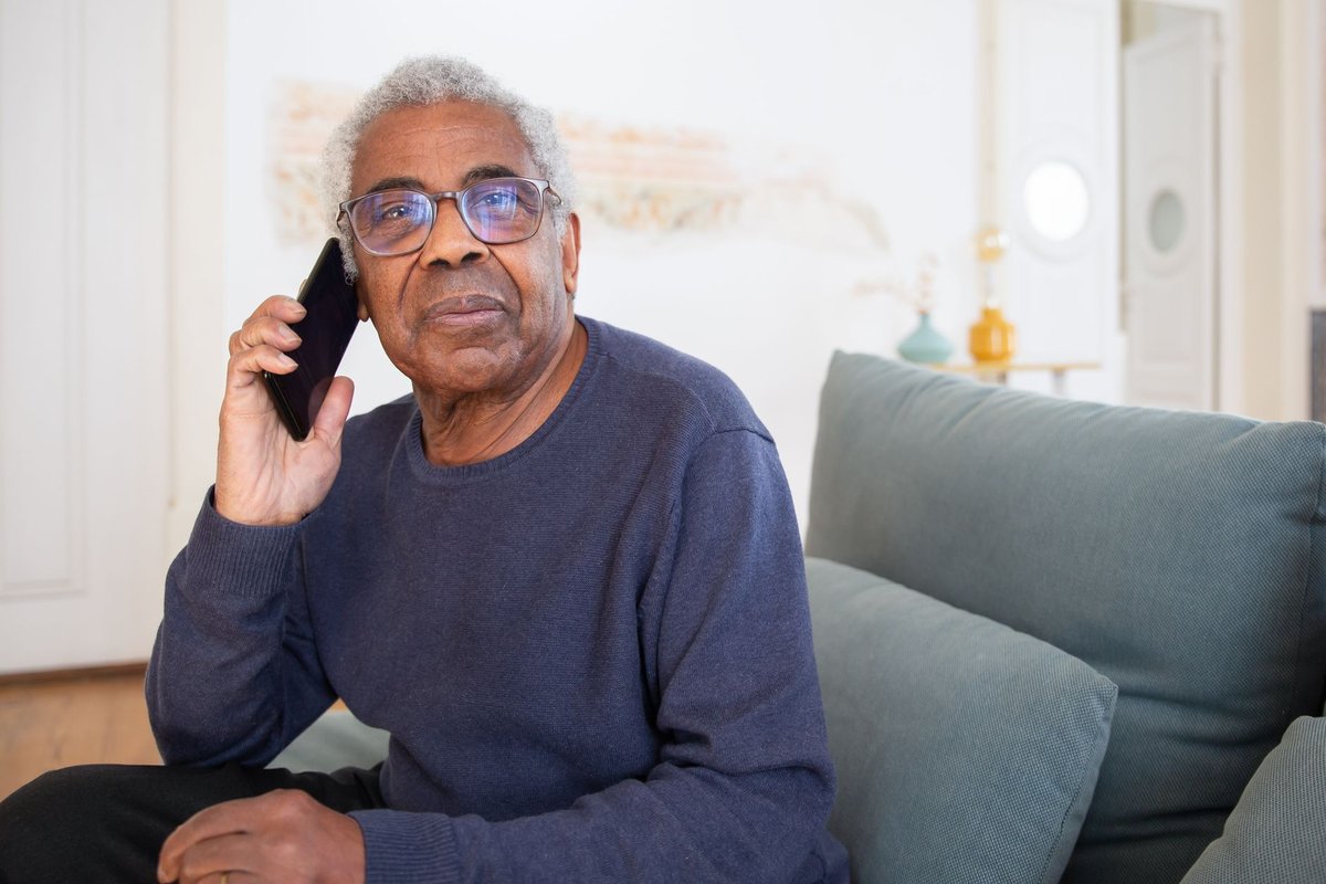 Older man in glasses sitting on a sofa at home talking on a mobile phone