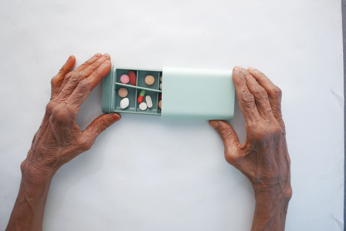 Older hands holding a small compartment box filled with pills of different colors